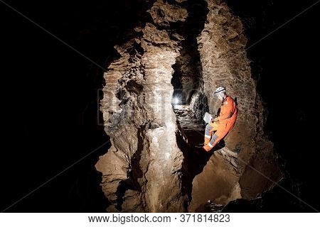 Man Walking And Exploring Dark Cave With Light Headlamp And Map In His Hand Underground.