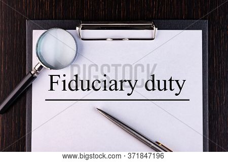Text Fiduciary Duty Is Written On A Notebook With A Pen And A Magnifying Glass Lying On The Table. B