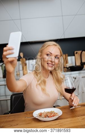 Focus Of Smiling Woman Taking Selfie On Smartphone Near Glass Of Red Wine And Plate With Thai Noodle