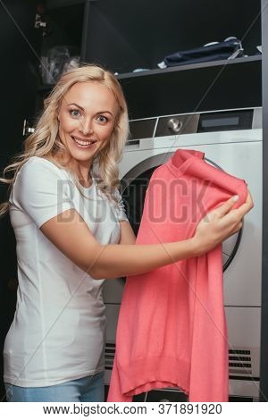 Housewife Looking At Camera While Holding Pullover Near Washing Machine