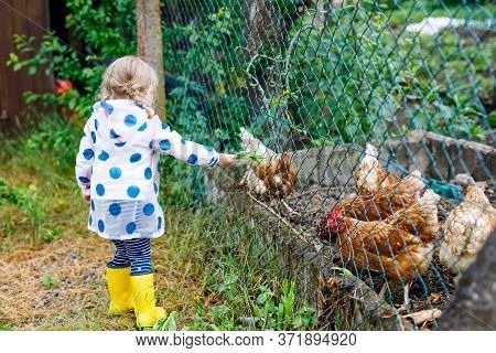 Outdoor Portrait Of Happy Smiling Little Toddler Girl Wearing Rain Jacket On Rainy Cloudy Day Feedin