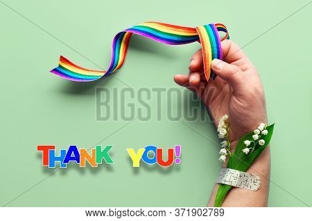 Rainbow Ribbon In Womans Hand. Chamomile Flowers And Grass Bouquet Attached To Wrist With Medical Pa