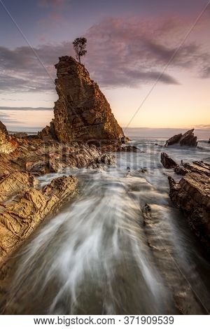Ocean Tides Flow Through A Narrow Chasm Beside Impressive Sea Stack Rock With One Sole Tree Growing 