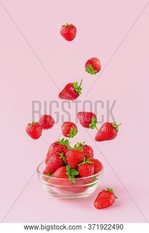 Flying Fresh Strowberries In Transparent Glass Bowl. Healthy Food On Light Pink Background. Deliciou