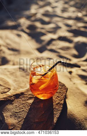 Orange Slice And Aperol Spritz Cocktail On A Stone Against The Backdrop Of A Sandy Beach. Glass With
