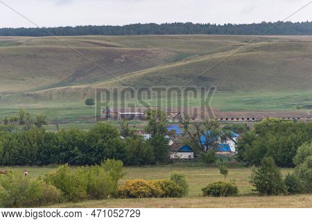Horse Grazing In A Field With A House In The Background, Hill On Background