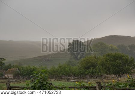 A Field With A Fence And A House In The Distance, Hills On Background. Rural Garden With Sunflowers 