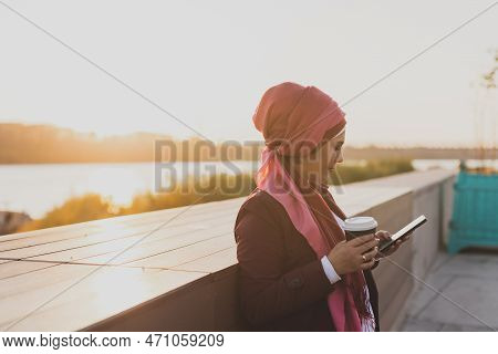 Modern Arab Girl In Hijab Walking By Street And Drinking Coffee Take Away In Spring Time Morning, Co