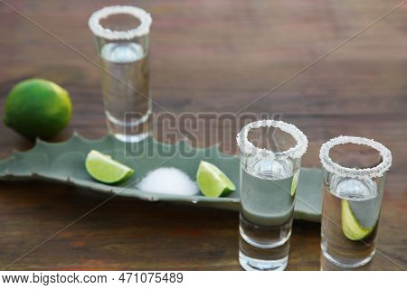Mexican Tequila Shots, Salt, Lime And Green Leaf On Wooden Table, Closeup. Drink Made Of Agava