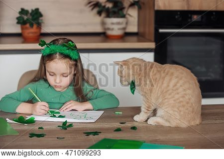 A Little Girl With A Bandage On Her Head Draws And Cuts Green Shamrocks For St. Patricks Day At A Ta