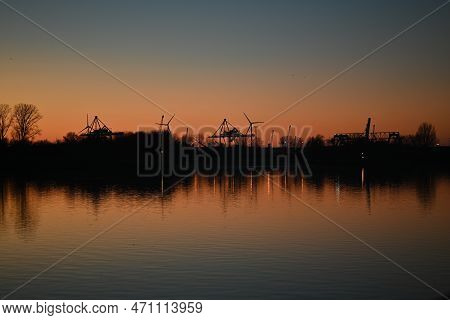 Evening Mood Besides A River Against A Containerport And Sunset