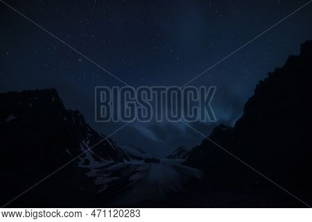 Awesome Mountain Landscape With Large Glacier Tongue And Black Silhouettes Of Rocks Under Clouds In 
