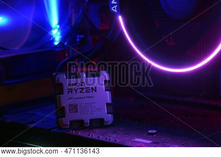 Close-up Of An Amd Ryzen 9 7900X Processor, Against The Backdrop Of Coolers With Light.