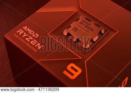 A Close-up Of An Amd Ryzen 9 7900X Processor In A Packaging Box With Backlit Keyboards In The Backgr