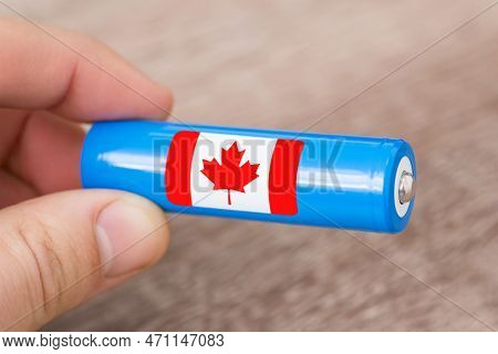 Close Up Shot Of Generic Li-ion Battery In Hands Of A Man, Flag Of Canada On Its Side. Concept Of Pr
