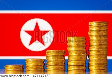 Money Coins Stacks In Rising Order In Front Of North Korea Flag. Development Of Economy Of North Kor