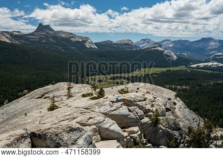 Hiker In Blue Hoodie Hunkers Down On The Windy Open Granite Of Lembert Dome In Yosemite