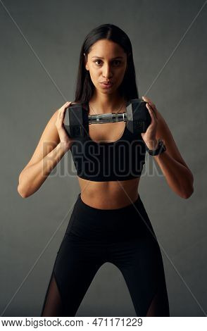 Focused Young Biracial Woman In Sports Bra And Leggings Exhaling While Holding Weights In Studio