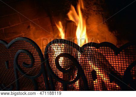 A Yellow-red Fire In The Fireplace Behind A Beautiful Wrought Iron Grate With Curls. Romantic Night 