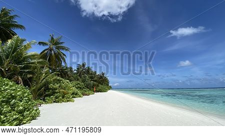 Paradise And Empty Beach With A Red Closed Umbrella, Clear Blue Water And Blue Partially Cloudy Sky 
