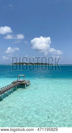Wooden Walkway Deck Over The Crystal Blue Ocean With A Boat Dock At The End And A Sunny Day With Som