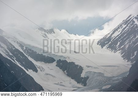 Atmospheric Mountain Landscape With Silhouettes Of Sharp Rocks And Sunlit Glacier In Low Clouds At C