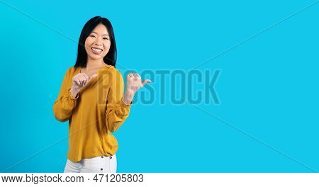 Cheerful Young Asiam Lady Pointing At Copy Space On Blue