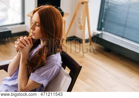 High-angle View Of Worried Young Woman Sincerely Praying With Eyes Closed Holding Folded Hands In Fr