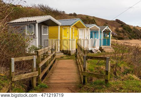 Coloured Beach Huts Above A Sandy Beach With Wooden Boadwalk For Access