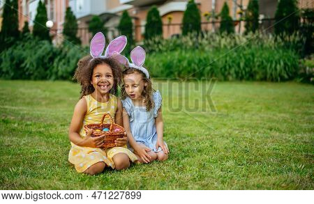 A Two Girls During Easter Egg Hunt And Putting Easter Eggs In Baskets