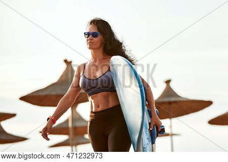 Woman Surfer With Surfboard Going To Surf At Seaside. Girl Holding Surfboard O And Goes To The Ocean