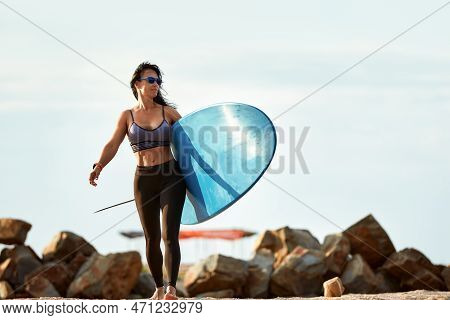 Woman Surfer With Surfboard Going To Surf At Seaside. Girl Holding Surfboard O And Goes To The Ocean