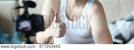 Athlete Man Holds Thumbs Up And Raises Dumbbells Sitting On Ball At Home In Front Of Camera. Recomme