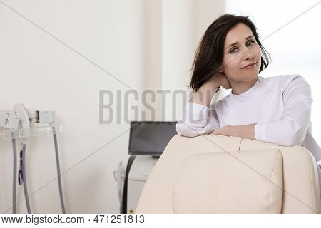 Relaxed Female Professional Doctor Posing In Doctor's Smock With Hands Folded In Front Against Inten