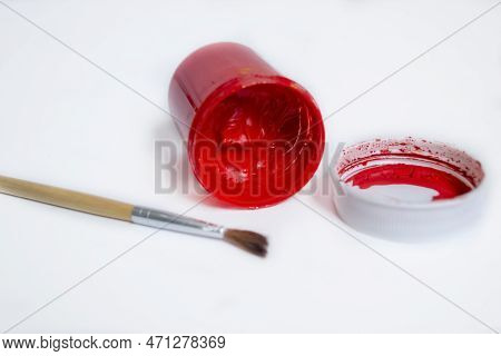 On The White Table Of The Jar Are Watercolors In Red. An Inverted Can Of Red Watercolor With A Brush