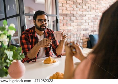 Young Diverse Loving Couple Eating Croissant And Talks Together At Home In Breakfast Time. Communica