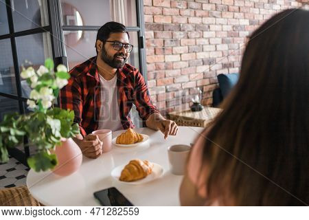 Young Diverse Loving Couple Eating Croissant And Talks Together At Home In Breakfast Time. Communica