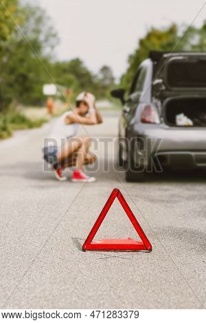 Young Beautiful Woman Spection A Rear Tire On The Side Of The Road. Car With Problems And Red Triang