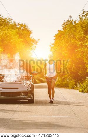 Young Sad Woman Standing Near The Road By The Broken Car In The Middle Of Nowhere. Smoke Coming Out