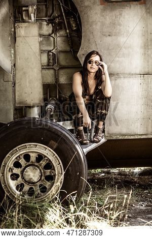 Portrait Of A Young Girl With Mimetic Military Dress Near The Old Abandoned Broken Plane. Concept Mi
