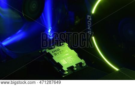 Close-up Of An Amd Ryzen 9 7900X Processor, Against The Backdrop Of Coolers With Light.