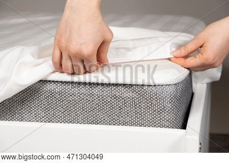 A White Satin Sheet With An Elastic Band Is Put On The Mattress Of The Bed, A Close-up Of The Hands.