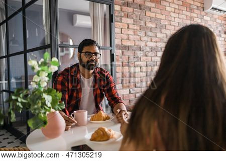 Young Diverse Loving Couple Eating Croissant And Talks Together At Home In Breakfast Time. Communica