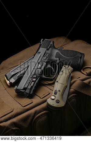 A Pistol, Cartridges For It And A Folding Knife On A Brown Backpack. Self-defense And Survival Kit. 