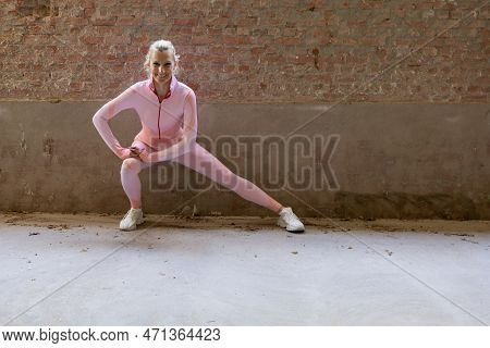 Beautiful Young Blonde Fitness Woman Wearing Pink Sports Clothes Stretching And Warming Up Quadricep