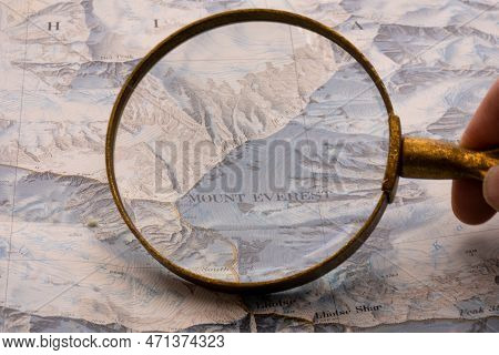 Hand Holding Magnifying Glass Showing Map Detail Of Mt. Everest On A Vintage Topographical Map. High
