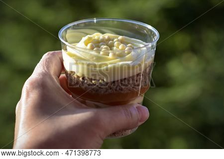 Sweet Dessert In Transparent Glass In Woman's Hand Against Green Background. Close-up. Trifle Is Del