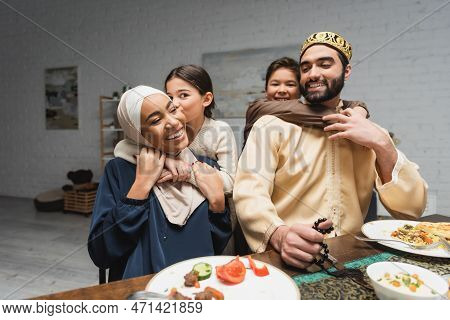 Smiling Muslim Children Hugging Parents During Ramadan Dinner At Home.