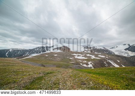 Dramatic Alpine Landscape With Large Snowy Mountain Dome In Sunlight Under Gray Cloudy Sky. Scenic P