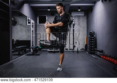A Young Sportsman In A Special Ems Suit Stretches And Warms Up His Muscles For Training Indoor Gym. 